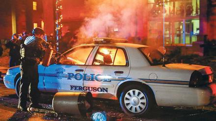 Brennende Wut. Ein Polizist versucht das Feuer zu löschen, das Protestierende in einem Polizeiauto in Ferguson gelegt haben.