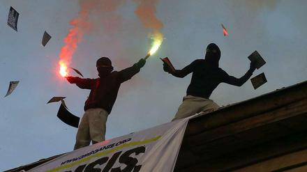 Berlin-Kreuzberg.  Teilnehmer einer "Revolutionären 1.-Mai-Demonstration stehen auf einem Dach und begleiten den Aufzug mit bengalischen Fackeln und Flugblättern.