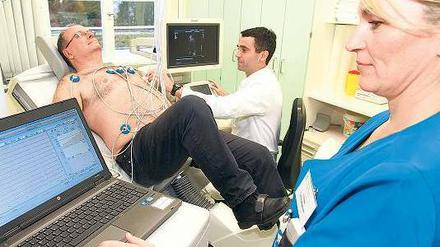 Peter Bobbert (M.) untersucht einen Patienten auf dem Fahrrad mit einer Stressechokardiographie.