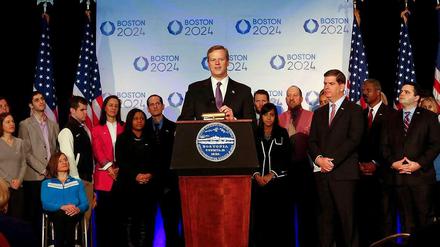 Charlie Baker, Governor von Massachusetts, steht bei der offiziellen Pressekonferenz zur Olympiabewerbung von Boston an einem Pult mit einem guten Dutzend weiterer Representanten in seinem Rücken.