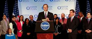 Charlie Baker, Governor von Massachusetts, steht bei der offiziellen Pressekonferenz zur Olympiabewerbung von Boston an einem Pult mit einem guten Dutzend weiterer Representanten in seinem Rücken.