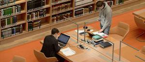 Zwei junge Männer schreiben und recherchieren in einer Bibliothek.