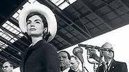 Jackie Kennedy mit hellen Handschuhen und einem cremefarbenen Krempenhut