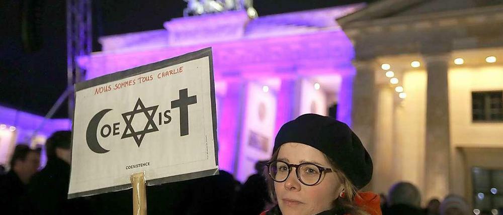 Eine Frau vor dem Brandenburger Tor mit einem Plakat, das die Gemeinschaft von Islam, Judentum und Christentum zeigen soll.