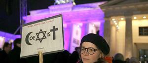 Eine Frau vor dem Brandenburger Tor mit einem Plakat, das die Gemeinschaft von Islam, Judentum und Christentum zeigen soll.