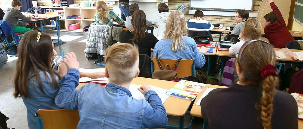 Schülerinnen und Schüler sitzen in einem Klassenraum, ein Lehrer schreibt etwas an die Tafel.