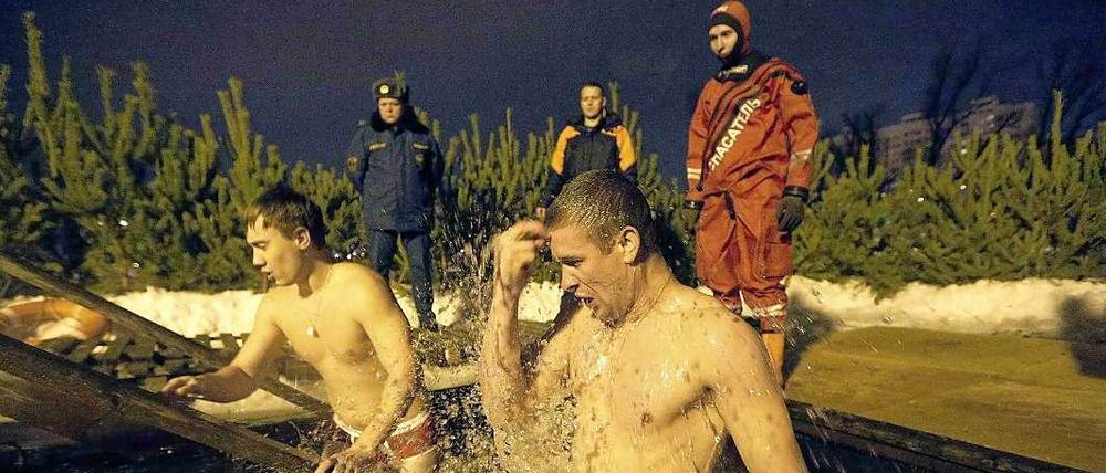 Ein Russe wäscht sich im Eisbad frei von Sünden. Polizei und Rettungsteams stehen bereit.