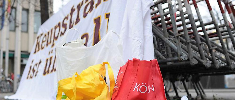 Eine Tasche mit der Aufschrift "Köln" steht vor einem Plakat mit der Aufschrift "Keupstraße ist überall", das vor dem Oberlandesgericht in München an Absperrgittern angebracht ist. Am 9. Juni 2004 explodierte in der Keupstraße in Köln eine vom NSU gezündete Nagelbombe.