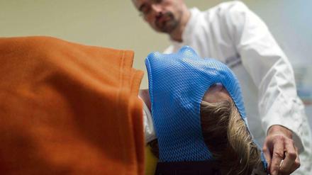Vor einer Strahlenbehandlung setzt ein Arzt der Patientin eine Schutzmaske auf.