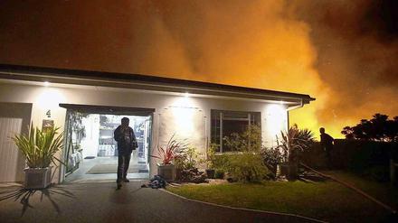 Ein Hausbesitzer in Kapstadt von seiner Garage. Im Hintergrund tobt ein Feuer, die Feuerwehr hat einen Schlauch durch den Garten gelegt. 