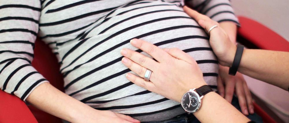 Hände einer Hebamme auf dem Bauch einer Schwangeren. 