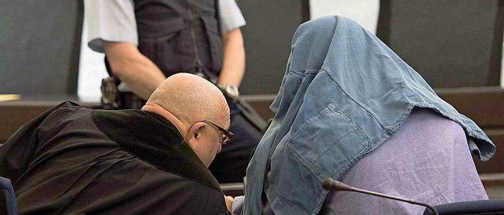 Der Angeklagte im Koffermord-Prozess, der eine Jacke über dem Kopf trägt, spricht am Dienstag in Stuttgart mit seinem Anwalt.