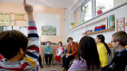 Schülerinnen und Schüler sitzen in einem Klassenraum im Kreis und sprechen mit einer älteren Frau.