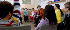 Schülerinnen und Schüler sitzen in einem Klassenraum im Kreis und sprechen mit einer älteren Frau.