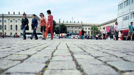 Vier junge Frauen und Männer gehen über einen Platz, in ihren Rücken ist das Hauptgebäude der Humboldt-Universität zu sehen.