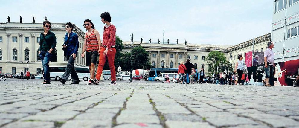 Vier junge Frauen und Männer gehen über einen Platz, in ihren Rücken ist das Hauptgebäude der Humboldt-Universität zu sehen.