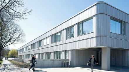 Studierende auf dem Weg in ein mit hellem Holz verkleidetes, zweistöckiges Gebäude.