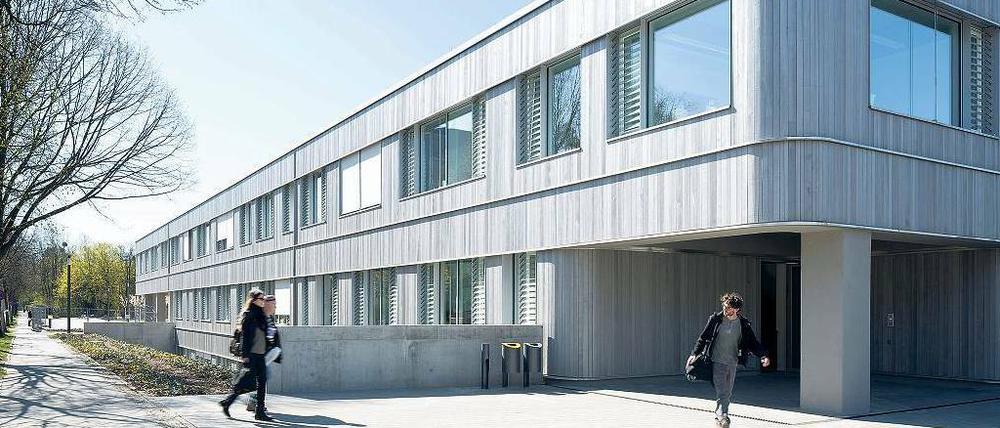 Studierende auf dem Weg in ein mit hellem Holz verkleidetes, zweistöckiges Gebäude.
