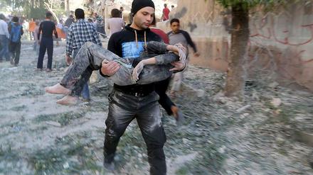 In Aleppo trägt am Sonntag, 3. Mai, ein Mann einen verletzten Jungen durch die Straßen. Eine Schule war Angaben von Aktivisten zufolge von einer Bombe des Assad-Regimes getroffen worden.