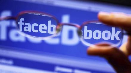 Facebook-Logo auf Computer-Bildschirm, gesehen durch eine vorgehaltene Brille.