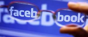 Facebook-Logo auf Computer-Bildschirm, gesehen durch eine vorgehaltene Brille.