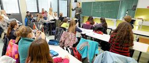 Ein Lehrer steht gestikulierend vor einer Schulklasse.