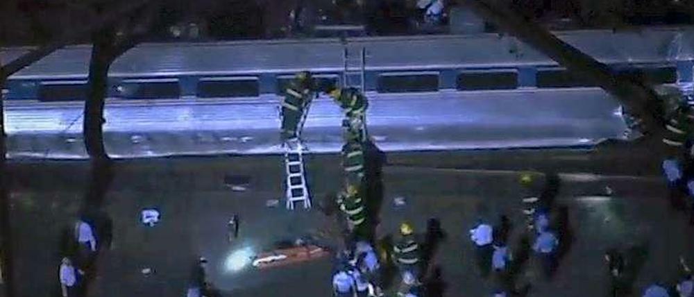 Rettungskräfte versuchen Passagiere aus einem umgestürzten Waggon zu retten. 