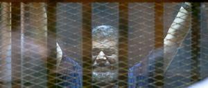 Ägyptens gestürzter Präsident Mohamed Mursi winkt aus dem Angeklagtenkäfig.
