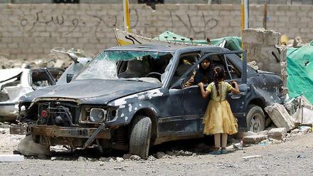 Eine Frau und ein Kind betrachten ein Auto, das bei den Luftangriffen der Militärallianz auf Sanaa zerstört worden ist. 