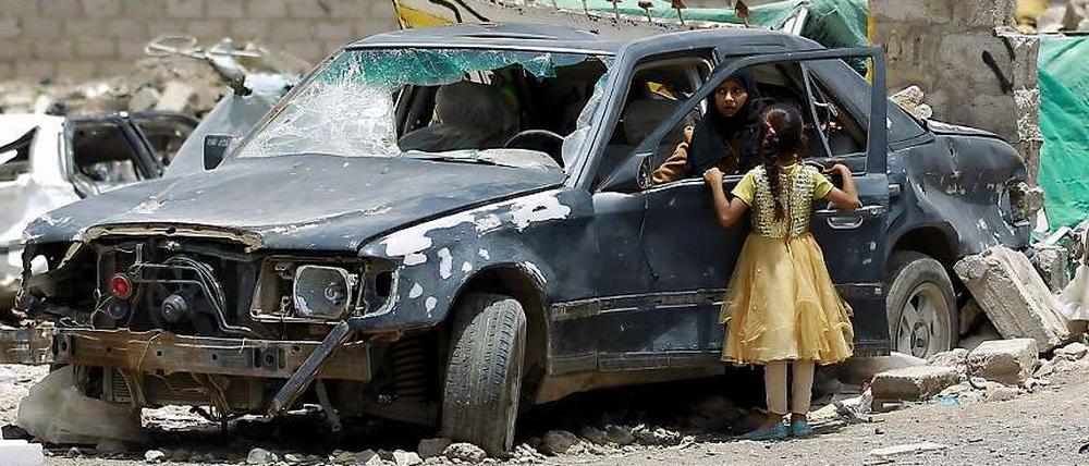 Eine Frau und ein Kind betrachten ein Auto, das bei den Luftangriffen der Militärallianz auf Sanaa zerstört worden ist.