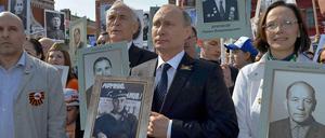 Kremlchef Wladimir Putin steht an der Spitze einer Demonstration, bei der Kinder und Enkel Fotos von Sowjetsoldaten aus dem Zweiten Weltkrieg hochhalten.