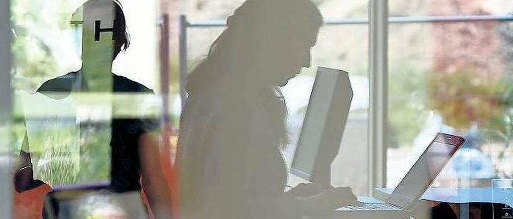 Hinter einer spiegelnden Glasscheibe arbeiten zwei Frauen in einer Bibliothek.