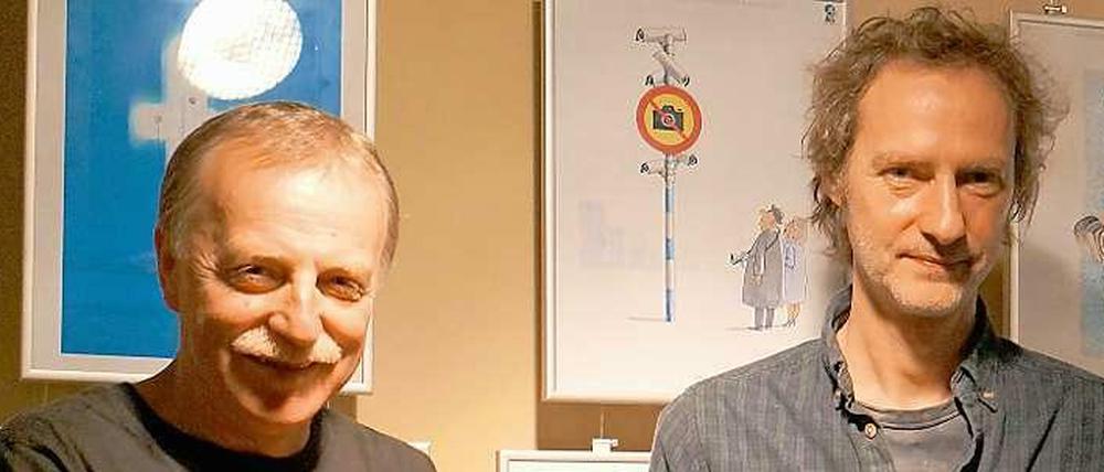 Einladung zur Karikaturenschau. Die Wettbewerbsveranstalter Valeriu Kurtu (li.) und Paul Gross mit dem Sieger-Cartoon.von Sergey Semendyaev.