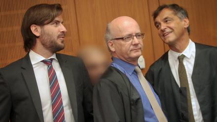 Der Angeklagte (2.v.l.) wird am Freitag im Landgericht in Frankfurt am Main von seinen Anwälten Andreas Groß (M) und Thomas Scherzberg (r) verdeckt. Der Angeklagte soll einen etwas älteren Rocker im April 2014 in Frankfurt mit 34 Schüssen und Schlägen grausam getötet haben.