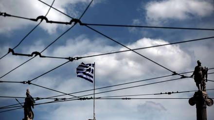 Athener Wirren. Die griechische Flagge, Athena (links) und Apollo durch die Oberleitungsdrähte einer Tram in der griechischen Hauptstadt gesehen.