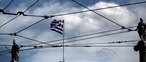 Athener Wirren. Die griechische Flagge, Athena (links) und Apollo durch die Oberleitungsdrähte einer Tram in der griechischen Hauptstadt gesehen. 
