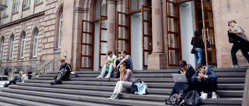 Studierende sitzen auf den Treppenstufen vor einem Eingang der Universität in Aachen.