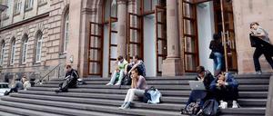 Studierende sitzen auf den Treppenstufen vor einem Eingang der Universität in Aachen.