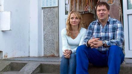 Charly Hübner und Christina Große sitzen vor dem Eingang eines Plattenbau-Wohnblocks in Schwerin.