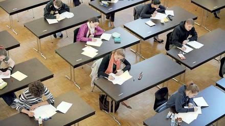 Schülerinnen und Schüler sitzen schreibend an Einzeltischen.