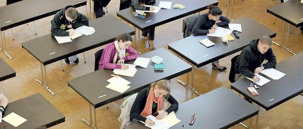Schülerinnen und Schüler sitzen schreibend an Einzeltischen.