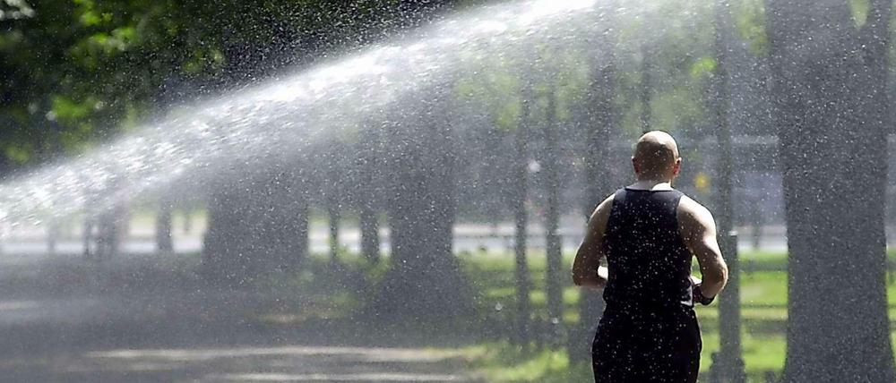 Abhilfe gegen die Trockenheit: Ein Jogger läuft im Tiergarten durch eine Sprenkleranlage.