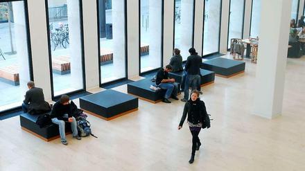 Junge Menschen sitzen im Foyer einer Universitätsbibliothek und schauen aus dem Fenster oder gehen quer durch den Raum.