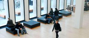 Junge Menschen sitzen im Foyer einer Universitätsbibliothek und schauen aus dem Fenster oder gehen quer durch den Raum.