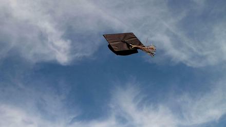 Ein Doktorhut, der in die Luft geworfen wurde, schwebt vor weißen Wolken am blauen Himmel.