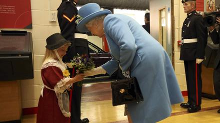 Queen Elizabeth bei ihrem Besuch in Wales. Kurz nachdem sie von dem Mädchen Blumen überreicht bekommt, wird dieses vom nebenstehenden Soldaten beim Salutieren von dessen Hand im Gesicht getroffen.