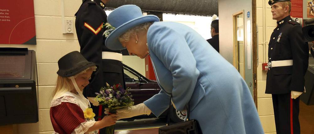 Queen Elizabeth bei ihrem Besuch in Wales. Kurz nachdem sie von dem Mädchen Blumen überreicht bekommt, wird dieses vom nebenstehenden Soldaten beim Salutieren von dessen Hand im Gesicht getroffen.