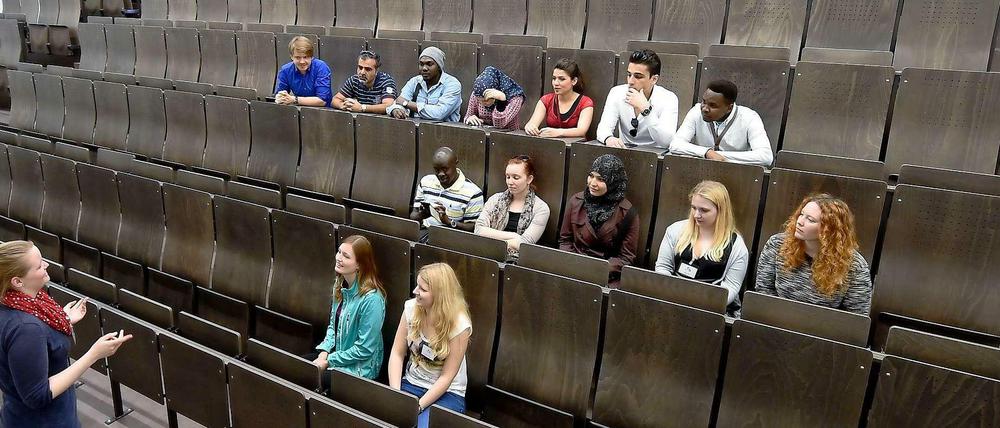 Studierende sitzen in einem Hörsaal, vor ihnen steht eine junge Frau und gestikuliert.