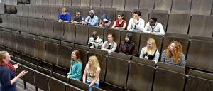 Studierende sitzen in einem Hörsaal, vor ihnen steht eine junge Frau und gestikuliert.