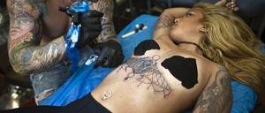 Eine Frau wird tätowiert. In Australien durfte eine Frau eine Zeitlang ihr Kind nicht stillen, weil die tätowiert war. Dieses Urteil hat das Gericht nun wieder annuliert. 